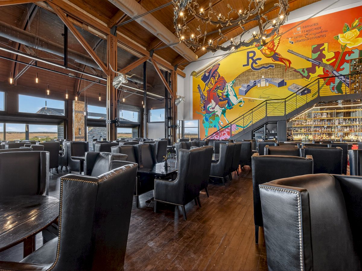 A stylish, modern restaurant with dark leather chairs, wooden floors, large windows, and a colorful mural on the wall.